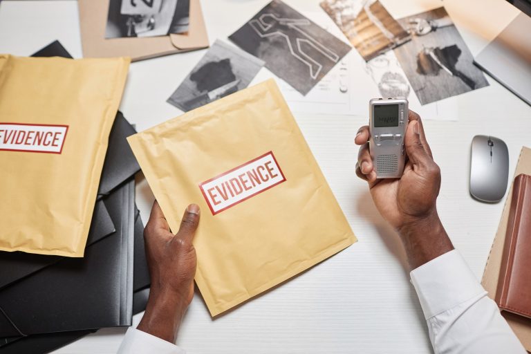 Top view detective with hands holding evidence folder and voice recorder at desk